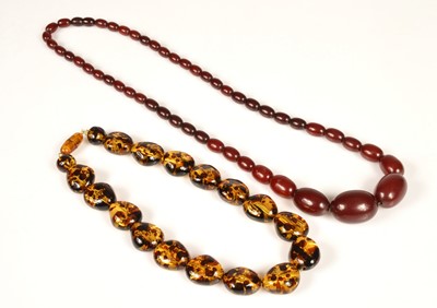 Lot 253 - A string of graduated 'cherry amber' oval bead necklace, with screw clasp, largest 3cm x 2cm, smallest bead 1.1cm x 0.7cm, 68cm maximum length, 53g, together with a resin pebble necklace