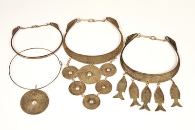 Lot 254 - Four Asian white metal torque necklaces, one with fish decoration, another with a collection of roundels each with engraved design and others 324g