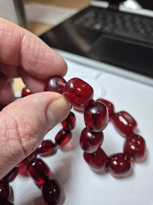 Lot 51 - A string of oval 'cherry amber' knotted strung beads