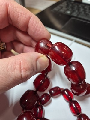 Lot 51 - A string of oval 'cherry amber' knotted strung beads
