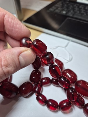 Lot 51 - A string of oval 'cherry amber' knotted strung beads
