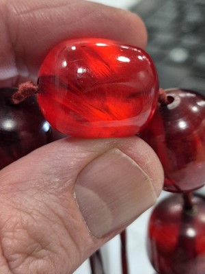 Lot 51 - A string of oval 'cherry amber' knotted strung beads